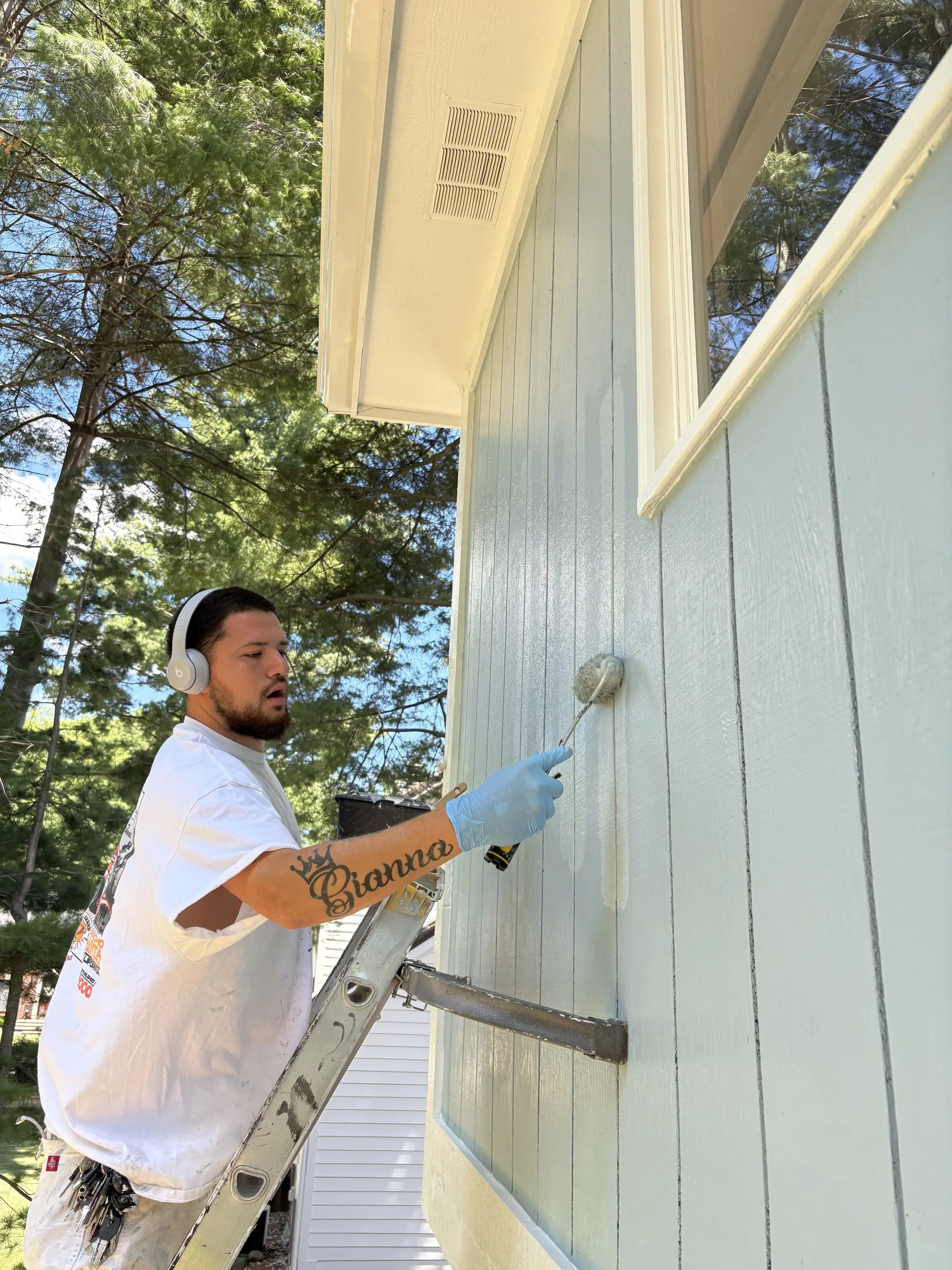 Painter on a ladder working a roller along board and batten siding beneath the soffit