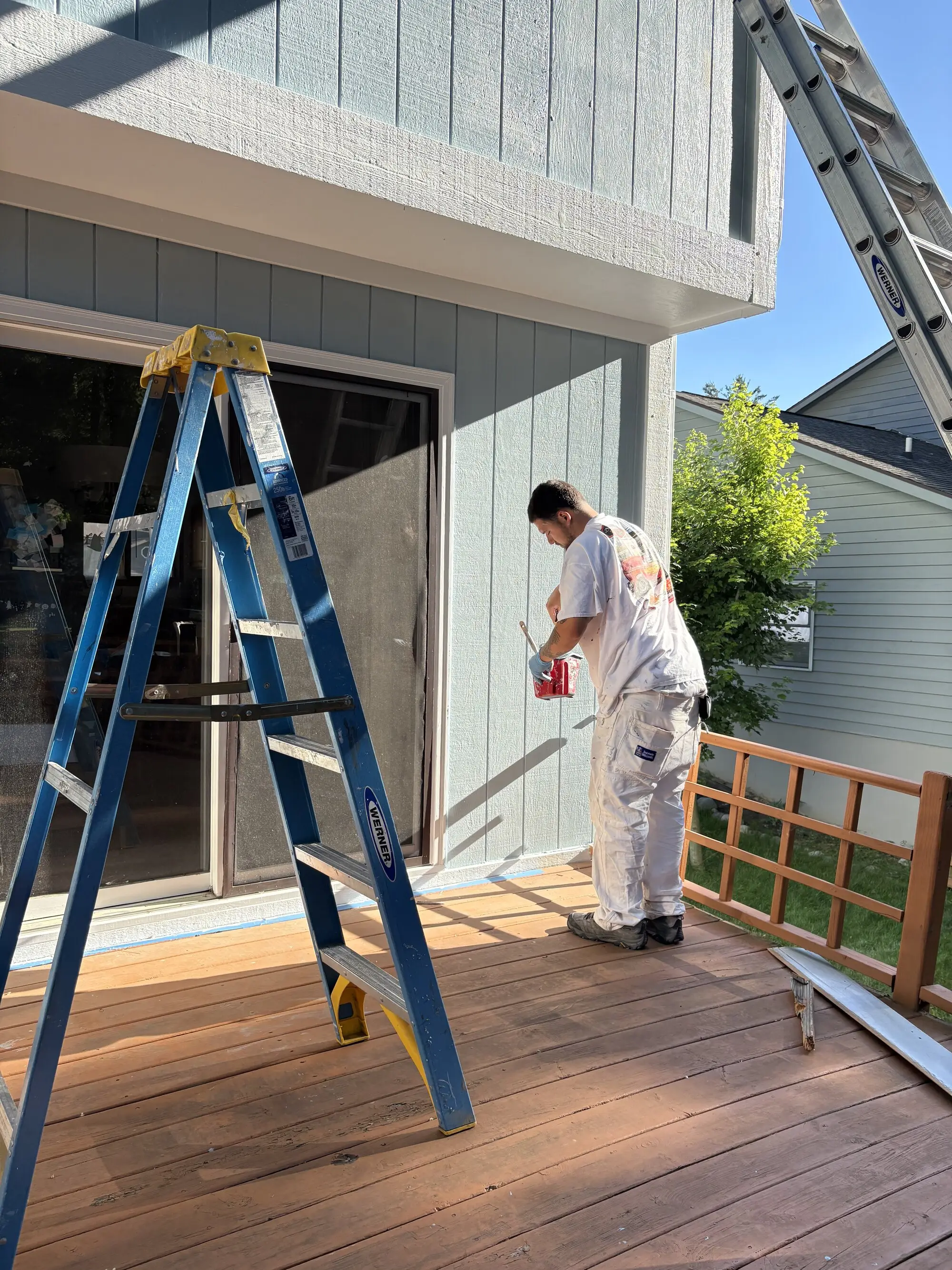 Painter working off a step ladder on a rear deck beside a sliding door