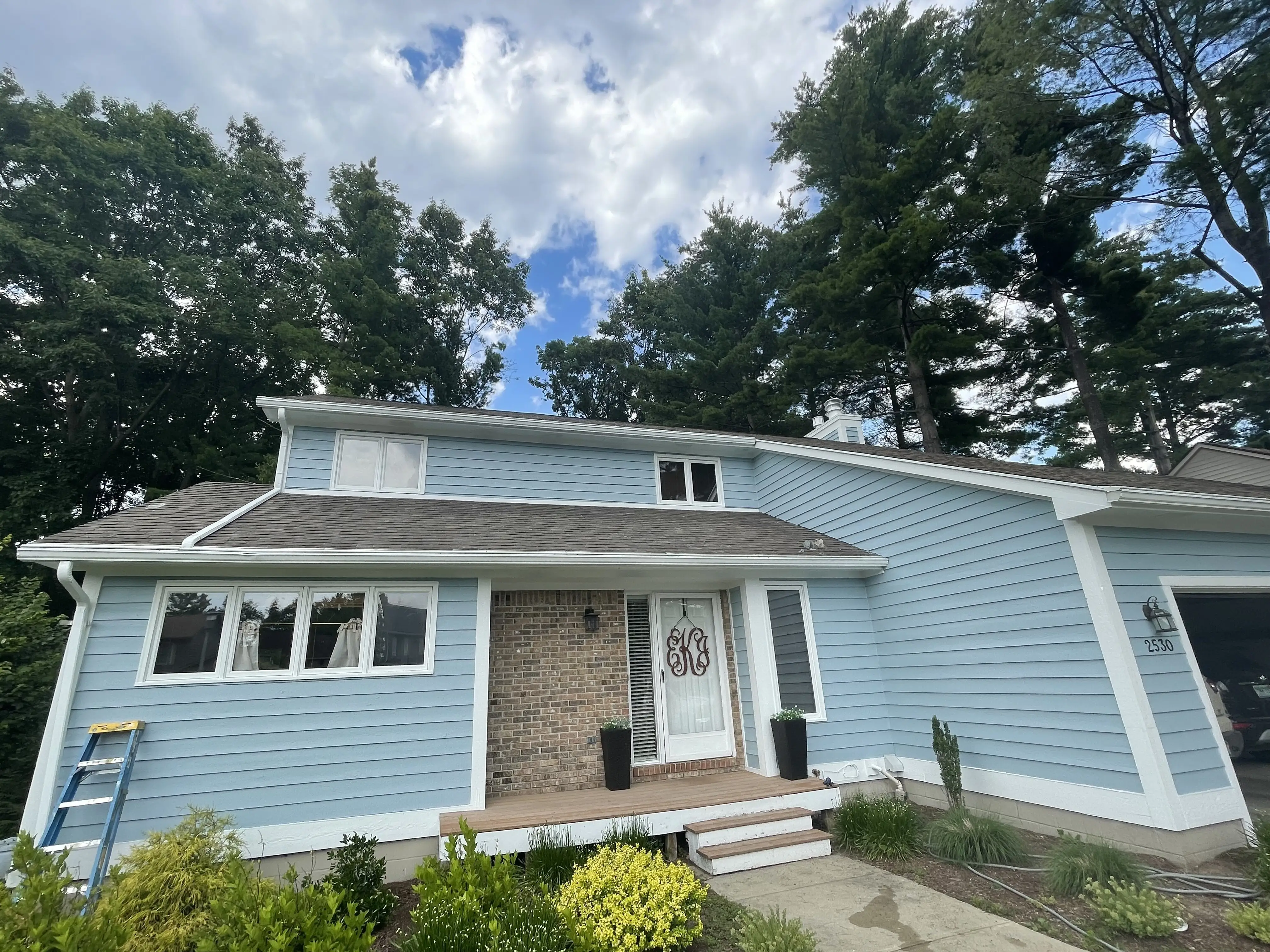 Painter on a ladder rolling pale blue siding up to the cream soffit and window trim