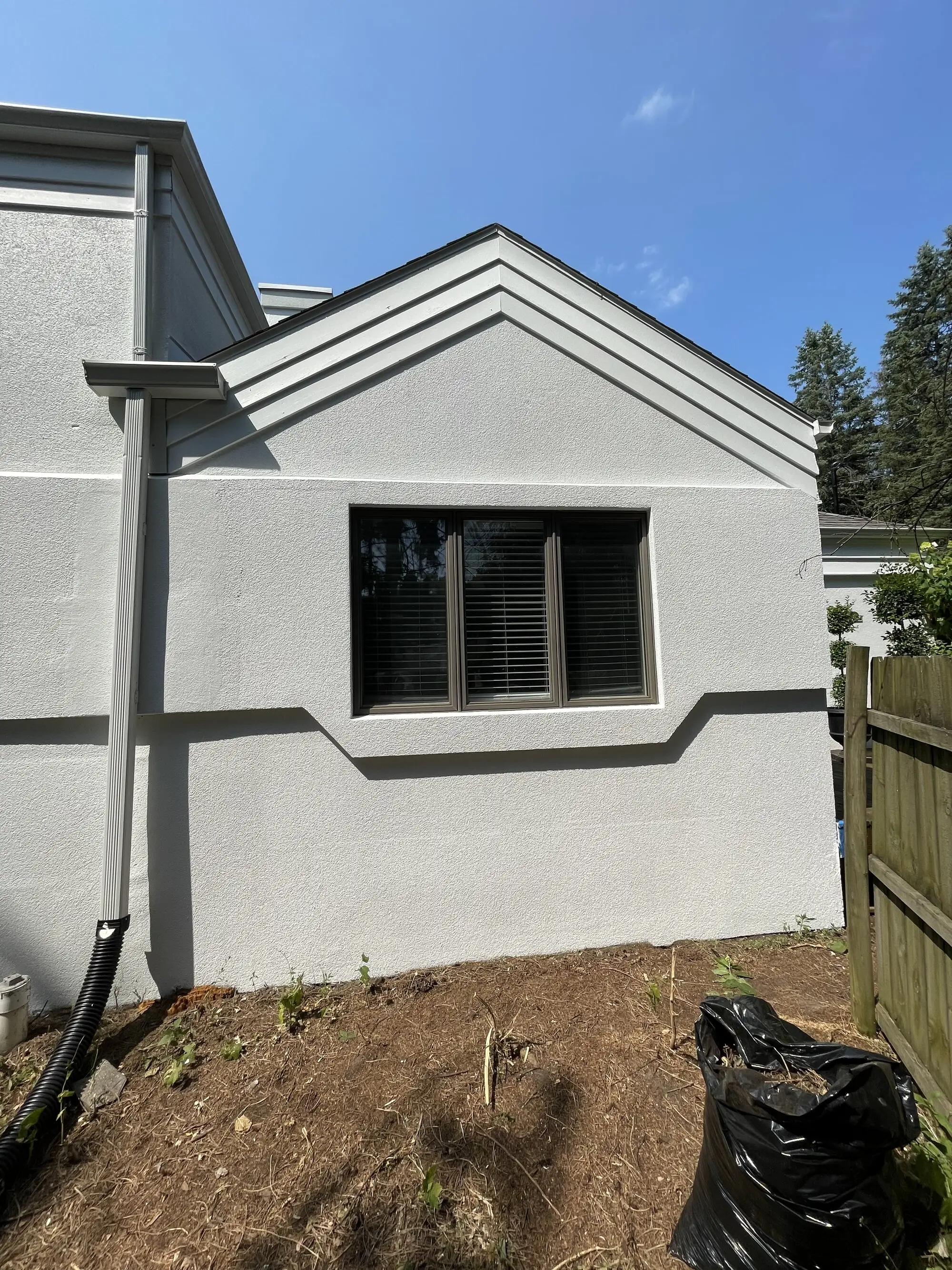Gray stucco gable with white banding and a dark framed window, freshly coated